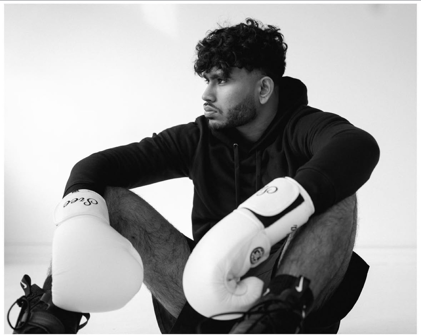 Black-and-white photo of Sree seated in a black hoodie and white boxing gloves, looking off to the side
