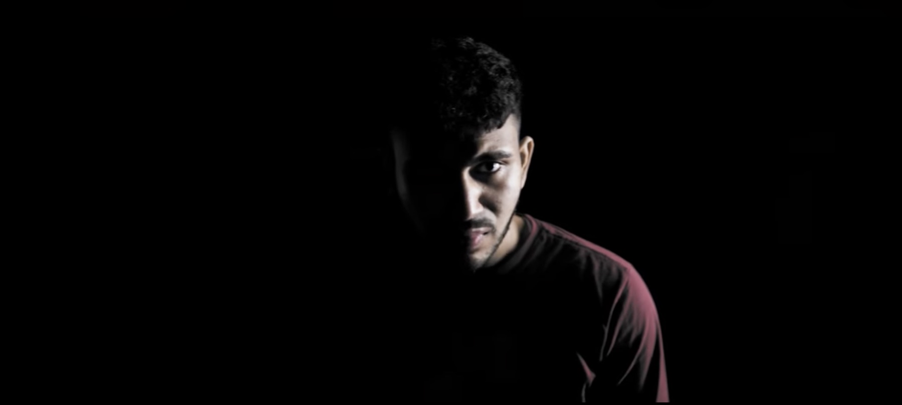 Sree as Benji, half his face lit against black, in the void scene