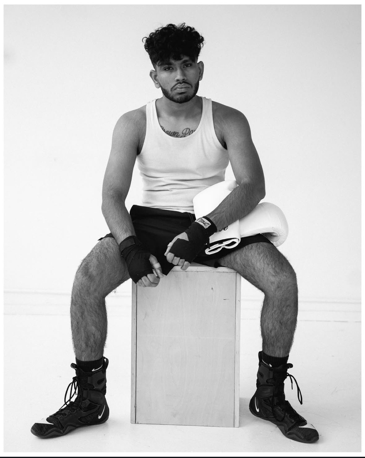 Sree seated on a wooden box in a tank top and hand wraps, looking into the camera