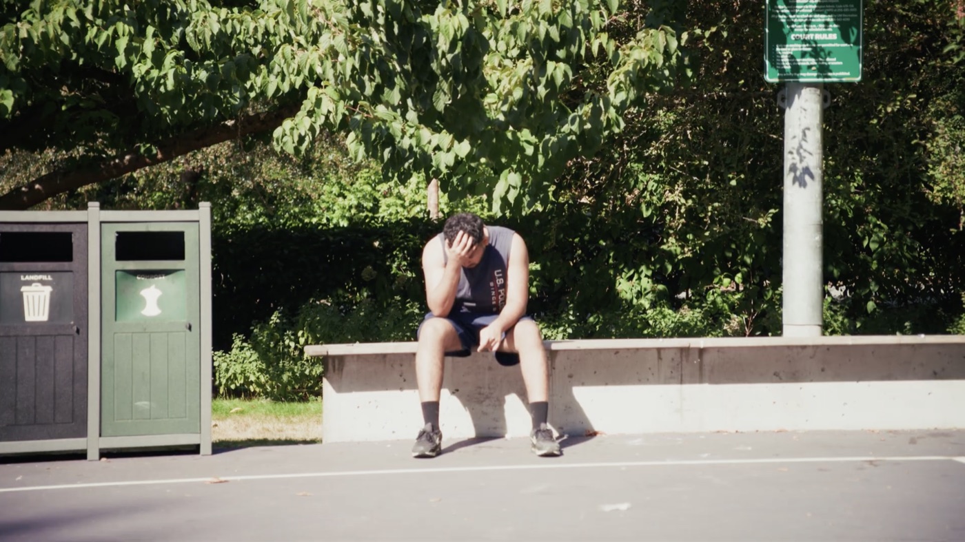 Sree as Sid alone on a bench beside a basketball court